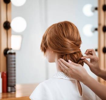 Female hairdresser making hairstyle to beautiful redhead girl in beauty salon. Copy space.