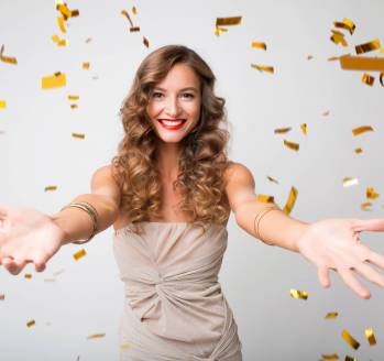 attractive young stylish woman celebrating new year, golden confetti flying, smiling happy, white background, isolated, wearing party dress, makeup and hairstyle